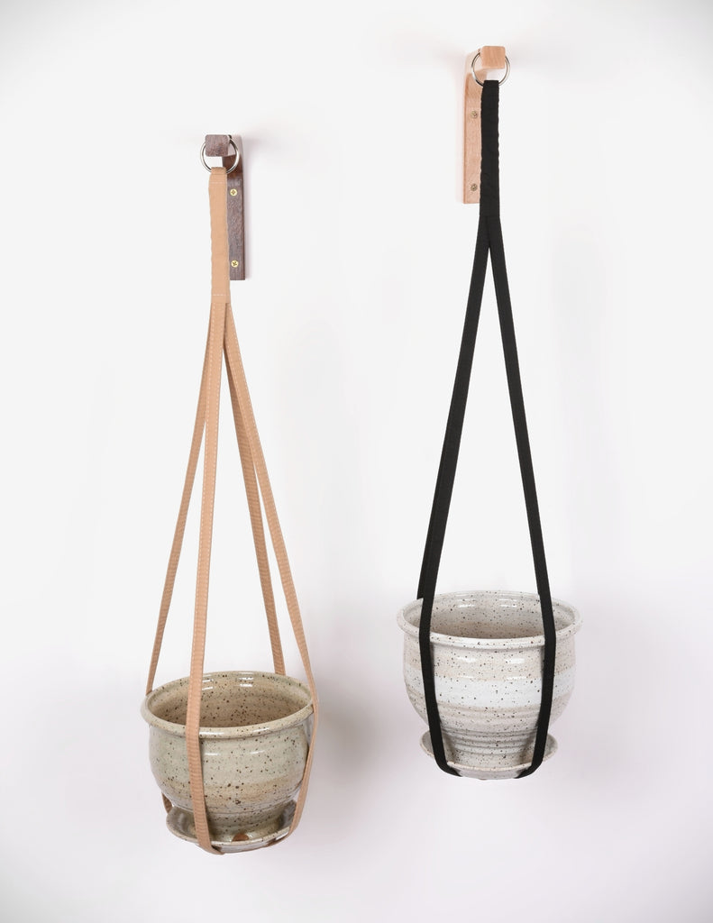 Tan and black plant hangers hanging from metal loops on wooden wall hooks